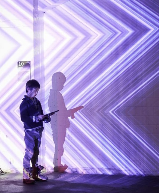 Ein kleiner Junge schaut auf ein Tablet. Der Hintergrund ist mit lila Mustern beleuchtet.